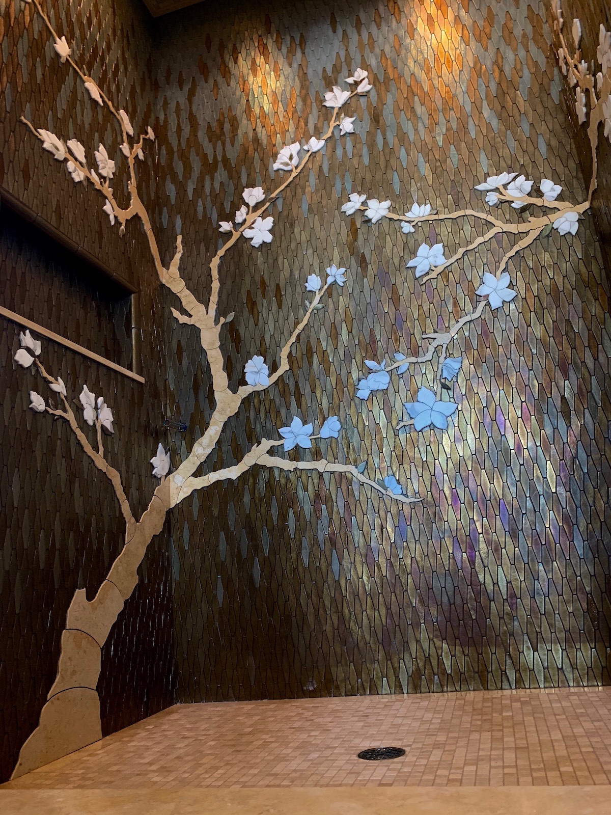 custom shower with glass mosaic and hand cut marble cherry tree inset into glass with a relief effect.